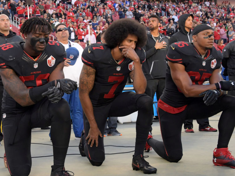 Colin Kaepernick (C), Eric Reid (R) et Eli Harold (L) s'agenouillent en signe de protestation pendant l'hymne national en octobre 2016 
