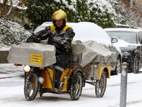  ] Une posteuse de l'opérateur suisse de courrier Schweizerische Post monte son trike électrique dans une rue enneigée à Zurich, en Suisse 