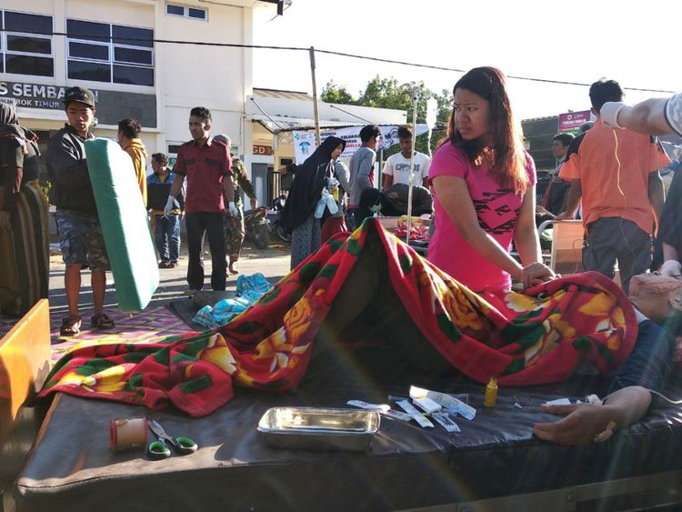 Une femme se tient près d'un blessé à l'extérieur d'un hôpital après qu'un séisme a frappé le village de Sembalun Selong à Lombok Timur