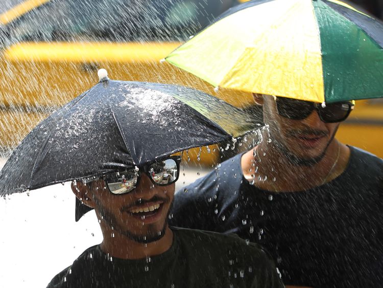 Des hommes irakiens portent des parapluies pour se protéger du soleil se lever sous une douche installée dans une rue de Bagdad à cause de la température élevée du 5 juillet 2018. - L'Irak connaît des températures très élevées et certaines villes du sud du pays ont été autorisé à prendre un jour de congé. (Photo par AHMAD AL-RUBAYE / AFP) (Crédit photo devrait lire AHMAD AL-RUBAYE / AFP / Getty Images)
