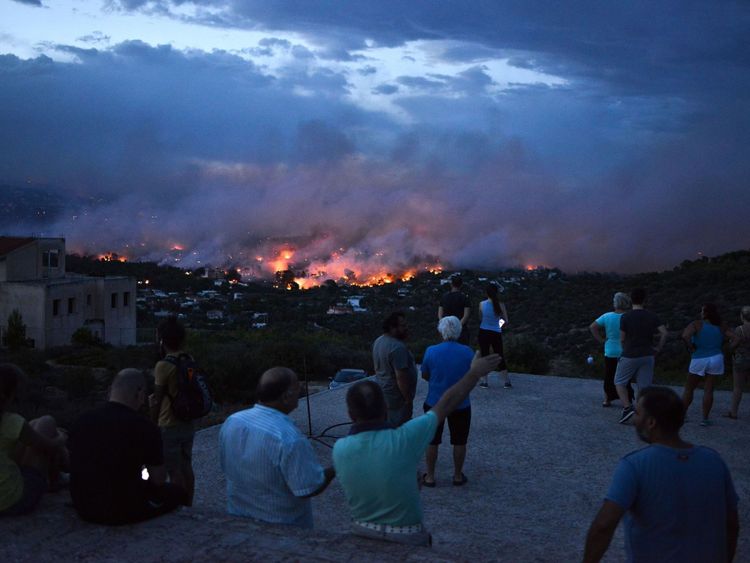 Les gens regardent un feu de forêt dans la ville de Rafina, près d'Athènes, le 23 juillet 2018
