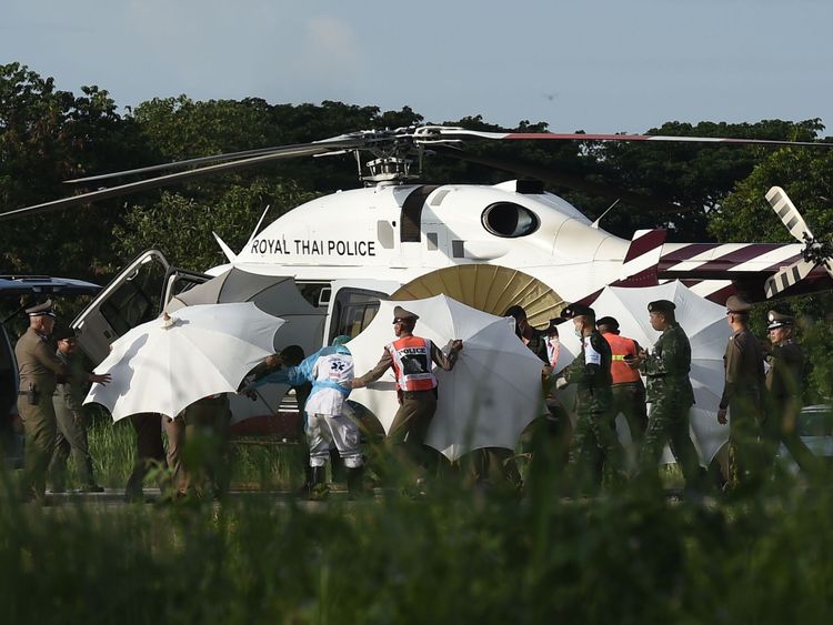La police utilise des parapluies pour couvrir une civière dans un aéroport militaire de Chiang Rai