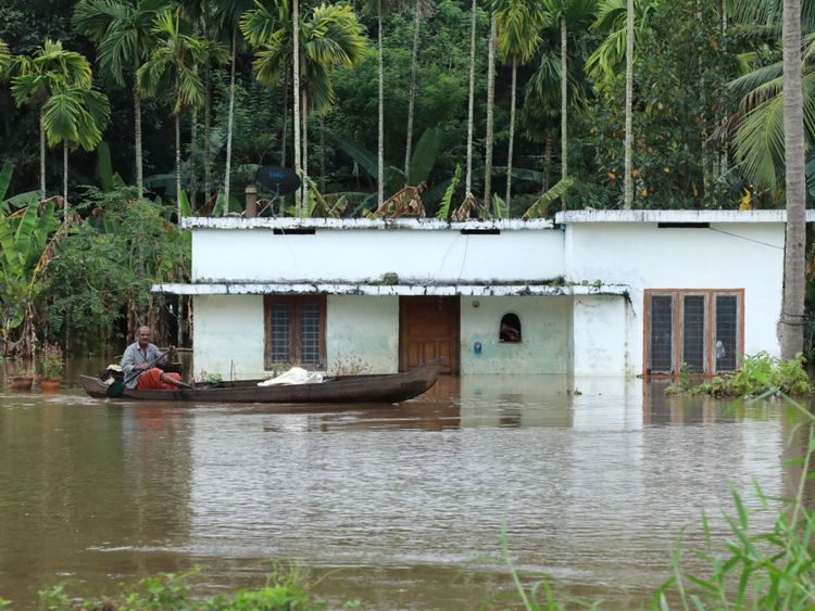 Un Indien monte à bord de son bateau à côté de maisons immergées dans les eaux de crue du district d'Ernakulam à Kochi, dans l'État indien du Kerala.