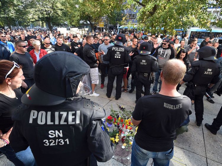 La police anti-émeute et des citoyens se tiennent à côté d'un mémorial de fortune pour un homme qui a été poignardé à mort