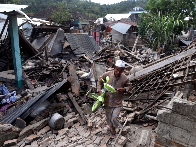 Un homme transporte un petit vélo à travers les ruines de maisons endommagées par un tremblement de terre à West Lombok, Indonésie, le 6 août 2018 sur cette photo prise par Antara Foto. Antara Foto / Zabur Karuru / via REUTERS ATTENTION EDITEURS - CETTE IMAGE A ETE FOURNIE PAR UN TIERS. CRÉDIT OBLIGATOIRE. INDONESIA OUT.