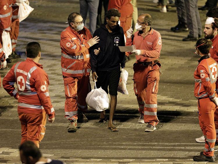 Un membre de la Croix-Rouge aide un migrant après avoir débarqué du navire des gardes-côtes italiens