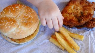 Une jeune fille mange un burger au poulet, des frites et du poulet frit.