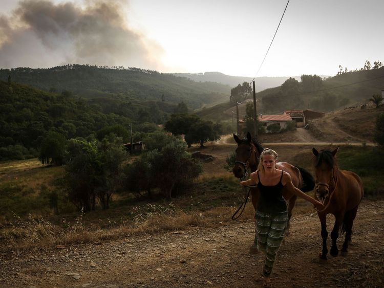 Une femme tire deux chevaux alors que des colonnes de fumée montent à la suite d’un incendie près de Monchique dans l’Algarve au Portugal, le 4 août 2018. - Un village dans une zone touristique du sud du Portugal a été évacué alors que plus de 400 pompiers les services ont dit. L’Europe étant toujours en état d’alerte au cours d’une vague de chaleur record et mortelle, le Portugal a vu le mercure atteindre près de 46 degrés Celsius - avec encore plus de jours chauds à venir. (Photo par CARLOS COSTA / AFP) (Crédit photo à lire 