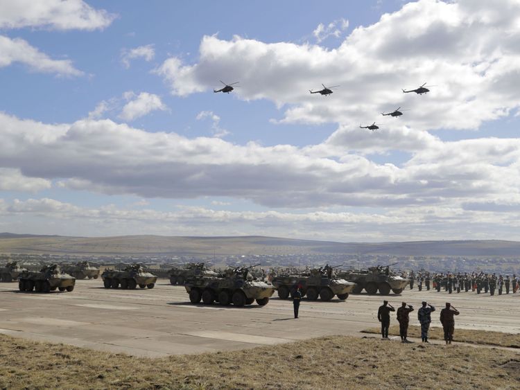Véhicules militaires et hélicoptères en mouvement lors d'un défilé sur un terrain d'entraînement