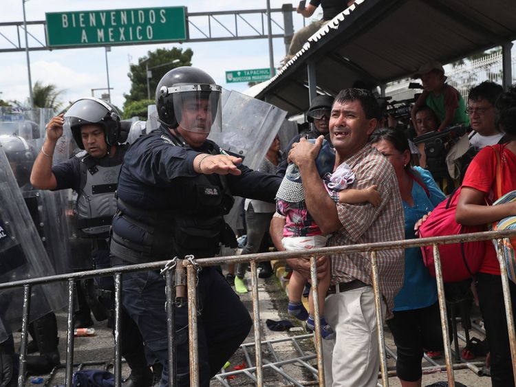 Un policier mexicain anti-émeute éloigne un père et son enfant d'un affrontement entre migrants et officiers
