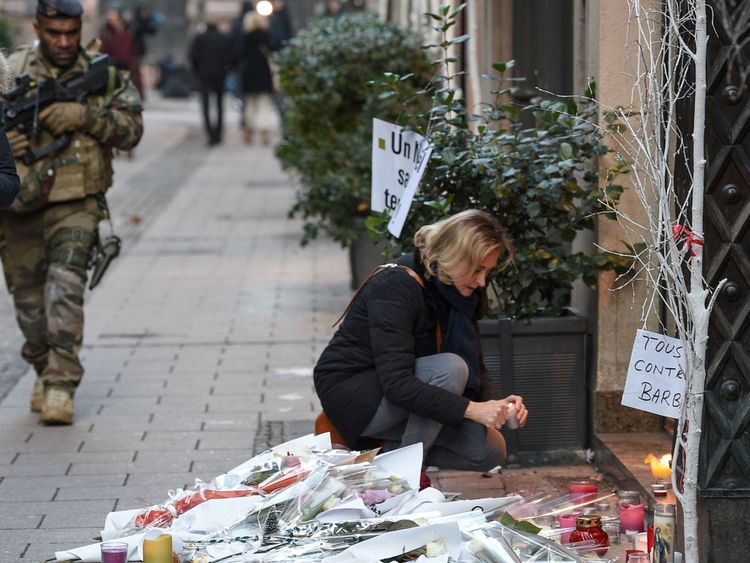 Un soldat français passe devant une femme allumant une bougie dans la rue