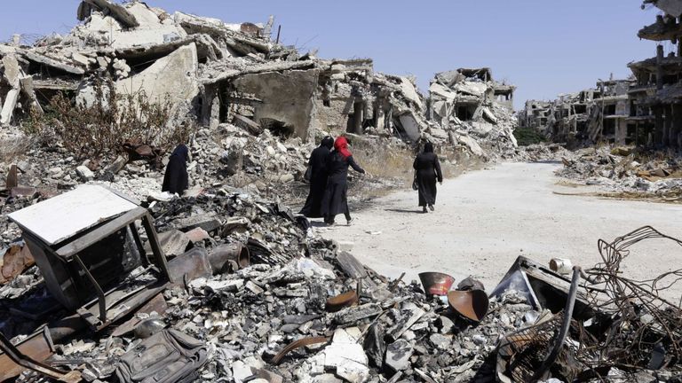 Trois femmes marchent dans des bâtiments détruits à Homs