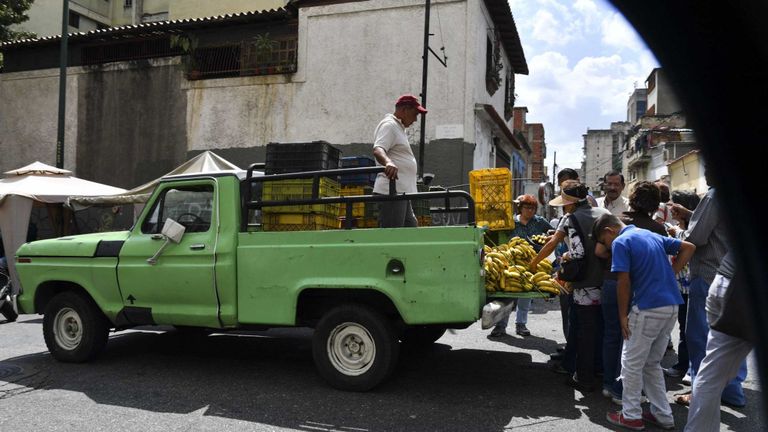 Les gens se rassemblent autour d'un homme vendant des bananes dans son camion dans un marché de rue de Caracas