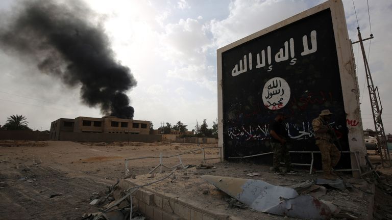 Un combattant irakien se tient près d'un mur portant le drapeau du groupe IS à Al Qaim