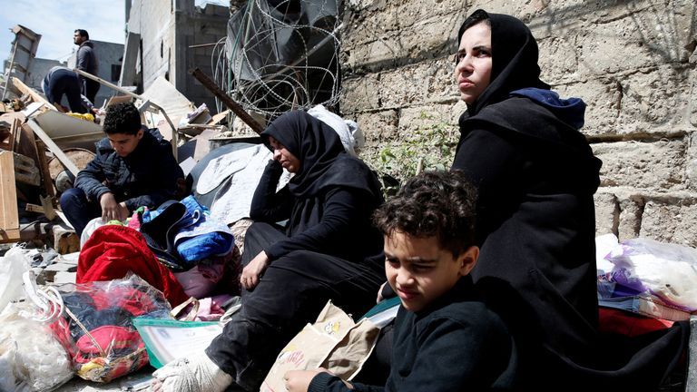 Des Palestiniens sont assis avec leurs affaires dans une rue devant leur maison détruite