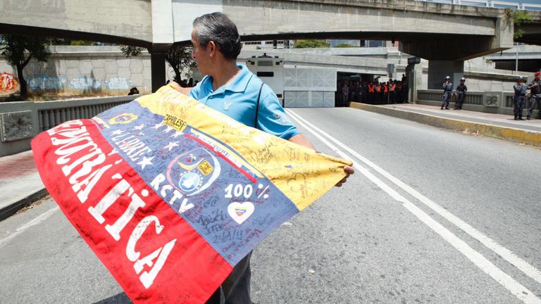 Un homme porte un drapeau vénézuélien devant un bloc de la police