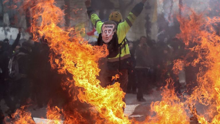 Un homme portant un masque de plaisanterie Emmanuel Macron sur le dos participe aux manifestations