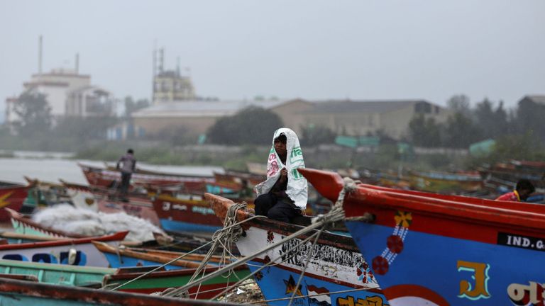 Un garçon se protège de la pluie alors qu'il est assis sur un bateau de pêche le long du rivage devant le cyclone Vayu à Veraval