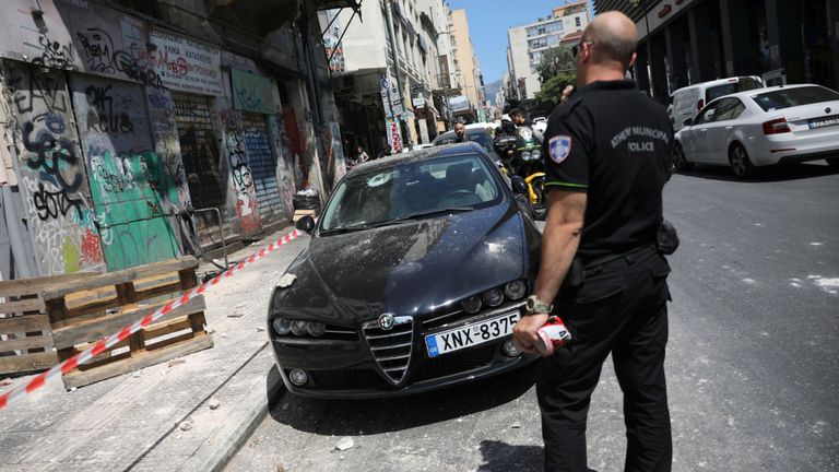 Un officier de police se tient dans une rue à côté d'une voiture endommagée à la suite d'un tremblement de terre à Athènes, en Grèce