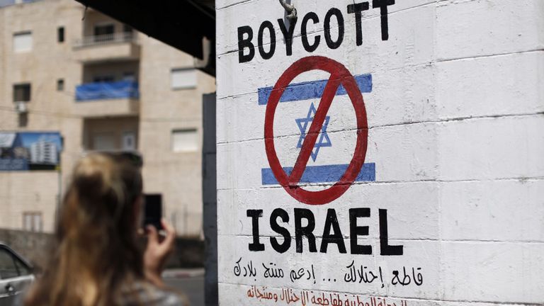 Un touriste photographie un panneau peint sur un mur de la ville biblique de Bethléem en Cisjordanie le 5 juin 2015, appelant à boycotter les produits israéliens provenant de colonies juives. La campagne internationale BDS (boycott, désinvestissement et sanctions), qui milite pour une interdiction des produits israéliens, vise à exercer une pression politique et économique sur l'occupation par Israël des territoires palestiniens afin de réitérer le succès de la campagne mis fin à l'apartheid en Afrique du Sud. 