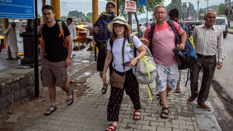 Les touristes portent leurs bagages alors qu’ils marchent sur les rives du lac Dal avant de quitter Srinagar 