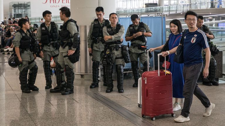 Les passagers passent devant la police surveillant l'entrée de l'aéroport international de Hong Kong