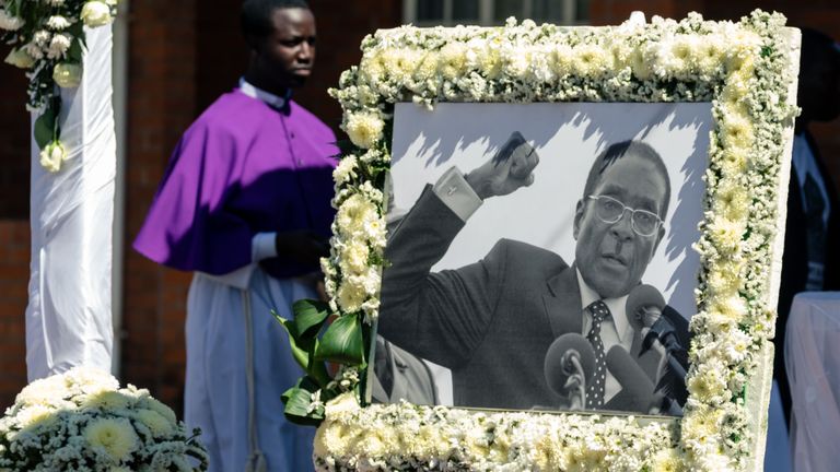 Un prêtre passe devant le portrait de Robert Mugabe lors de l'enterrement de l'ancien dirigeant du Zimbabwe dans son village natal à Kutama, le 28 septembre 2019