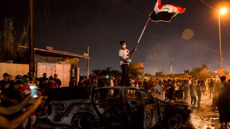 Un manifestant brandit un drapeau national alors qu'il se trouve sur un véhicule de police incendié à Basra