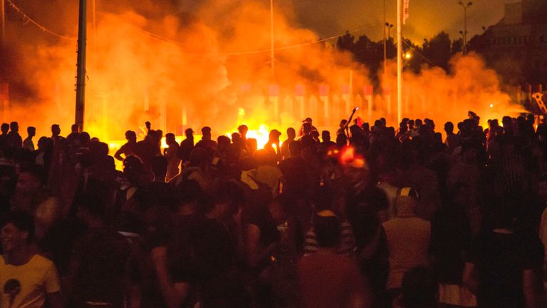 Les manifestants passent devant les feux dans la rue devant le siège du gouvernement local à Bassorah