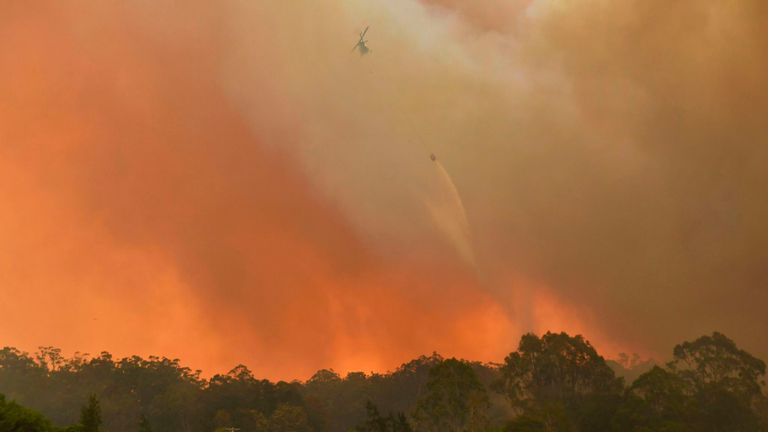 Un hélicoptère lâche de l'eau sur une propriété familiale alors que des feux de brousse frappent des terres agricoles près de la petite ville de Nana Glen, à quelque 600 km au nord de Sydney, le 12 novembre 2019.
