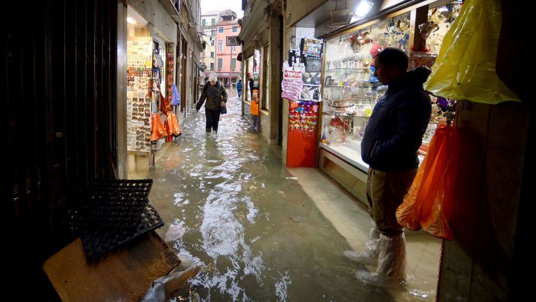 Un homme se tient devant une boutique de souvenirs pendant qu'une femme traverse une ruelle inondée