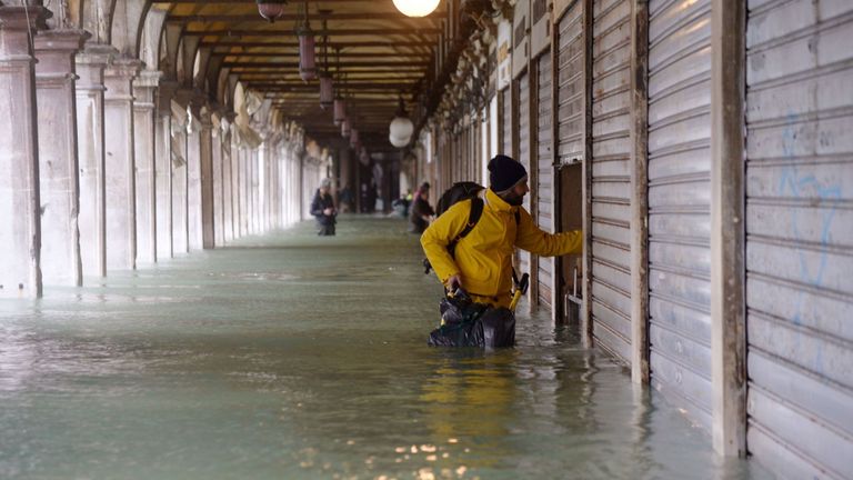 Un homme se tient près d’un magasin fermé dans une arcade inondée près de la place Saint-Marc 