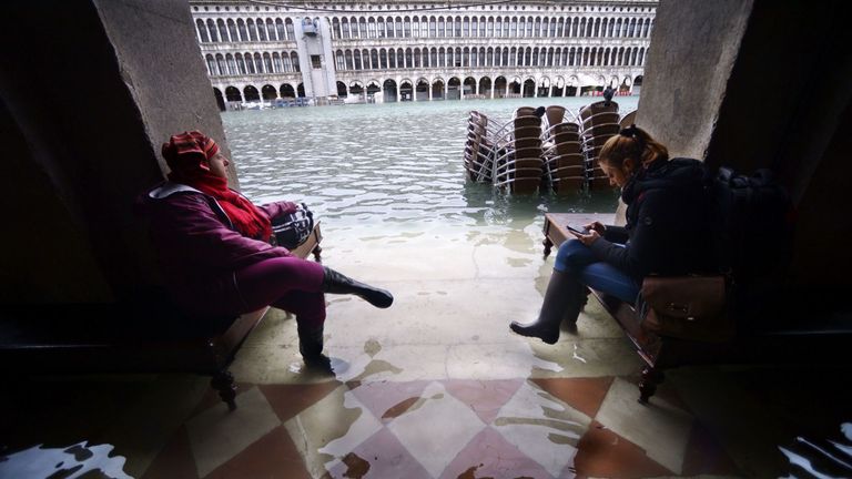 Les gens sont assis sur des bancs dans une arcade inondée près de la place Saint-Marc
