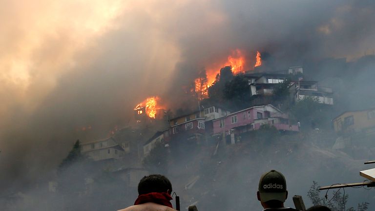 Des hommes regardent des maisons en feu lors d'un incendie de forêt sur la colline de Rocuant à Valparaiso, au Chili, le 24 décembre 2019. - Une cinquantaine de maisons ont été touchées par un incendie de forêt mardi à Valparaiso, où une alerte rouge a été déclarée. (Photo de RAUL ZAMORA / ATON CHILI / AFP) / Chili OUT / RESTREINT À UN USAGE ÉDITORIAL - CRÉDIT OBLIGATOIRE 