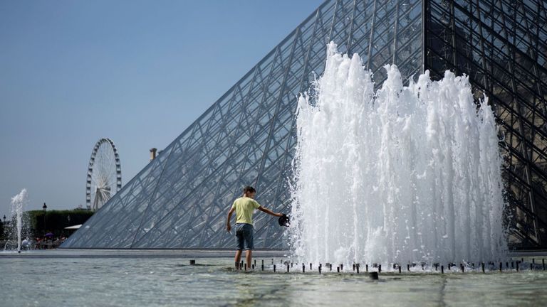 Un enfant se rafraîchit dans la fontaine de la pyramide du Louvre à Paris