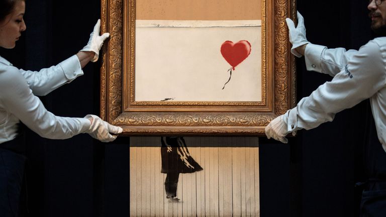 Les employés de Sotheby posent avec & quot; L'amour est dans le bac & quot; par Banksy 