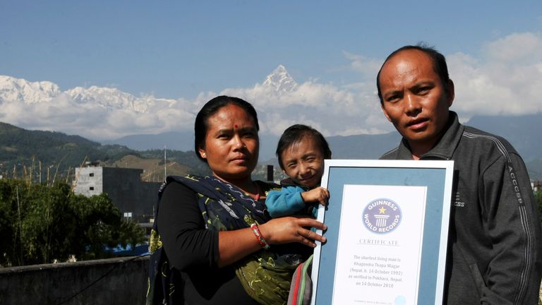Le Népalais Khagendra Thapa Magar (C), le plus petit homme du monde, pose avec ses parents Rup Bahadur Thapa Magar (R) et sa mère Dhana Maya Thapa (L) tout en tenant son certificat d'enregistrement Guiness dans le contexte du mont Machchhapuchhre à leur domicile à Pokhara, à environ 200 km à l'ouest de Katmandou, le 29 octobre 2010. Magar a été officiellement reconnu comme l'homme le plus petit du monde par le Livre Guinness des records le 14 octobre 2010 à l'âge de 18 ans. Khagendra Thapa Magar ne mesure que 67,48 centimètres (26,4 pouces) grand, selon les mesures finales prises par Guinness World Records. AFP PHOTO / Prakash MATHEMA (Le crédit photo doit se lire PRAKASH MATHEMA / AFP via Getty Images)