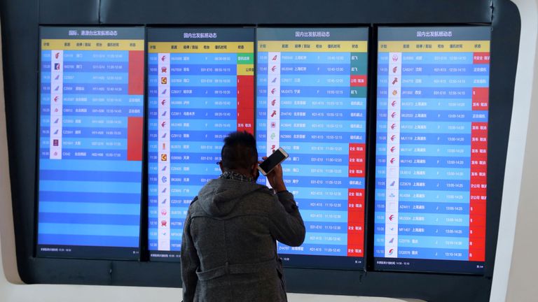Un homme se tient devant un écran montrant que plusieurs vols de départ ont été annulés dans un aéroport de Wuhan, dans la province du Hubei