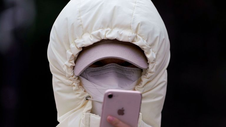 Une femme portant un masque et sa capuche serrée vérifie son téléphone à Shanghai
