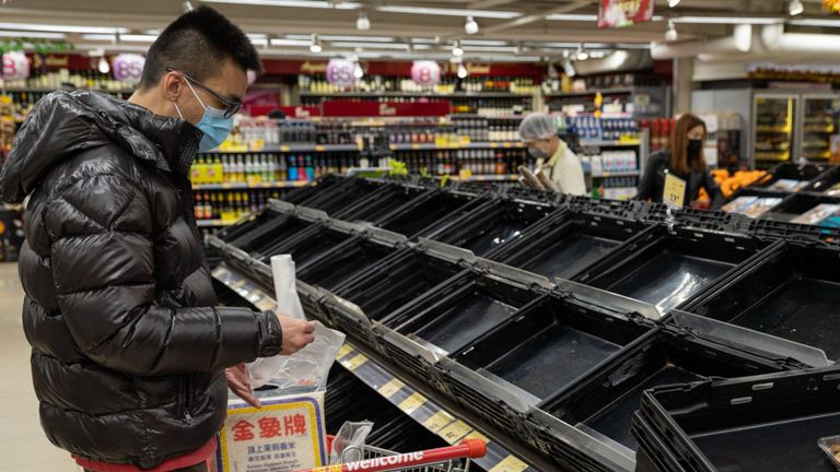 Un homme porte un masque facial alors qu'il se tient à côté d'étagères de légumes frais vides dans un supermarché à Hong Kong, Chine
