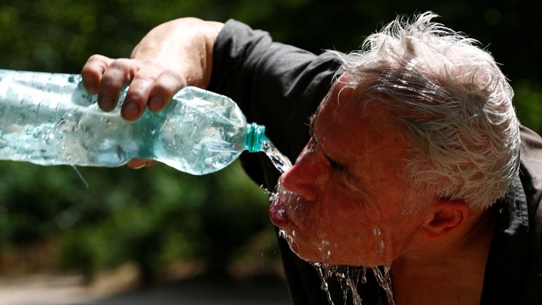 Un homme se refroidit avec une bouteille d'eau sur une chaude journée d'été dans un parc à Bruxelles, Belgique