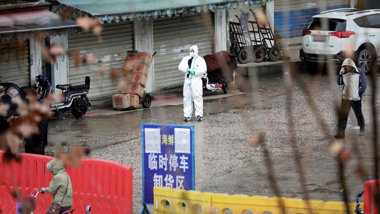 Un travailleur en tenue de protection se tient à l'extérieur du marché fermé des fruits de mer de Wuhan