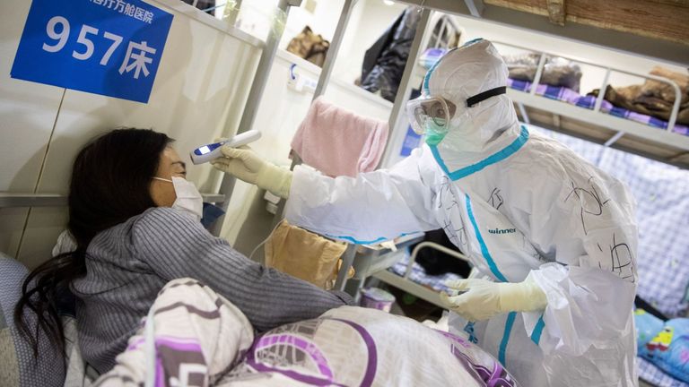 Le personnel médical vérifie la température d'un patient présentant des symptômes légers de COVID-19 dans un centre d'exposition transformé en hôpital à Wuhan