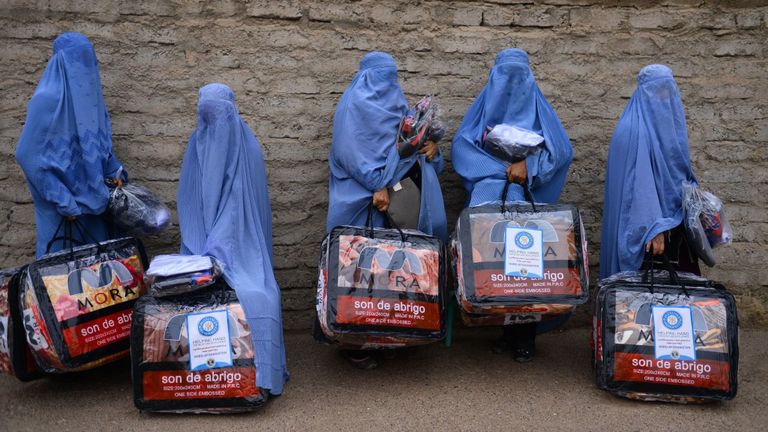 Sur cette photo prise le 19 décembre 2019, des femmes afghanes vêtues de burqa se tiennent debout avec des articles d'aide reçus d'un organisme de bienfaisance à Herat
