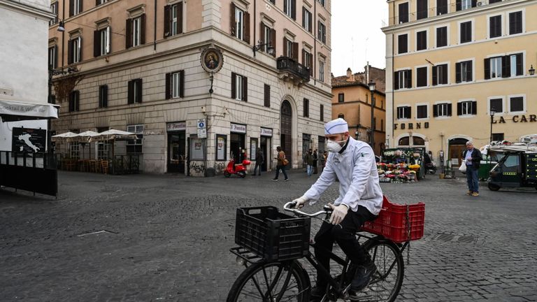 Un cuisinier portant un masque respiratoire dans le cadre des mesures de précaution contre la propagation du nouveau coronavirus COVID-19, fait du vélo sur une place déserte de Campo Dei Fiori au centre-ville de Rome le 10 mars 2020, alors que l'Italie imposait des restrictions nationales sans précédent à ses 60 millions 10 mars pour contrôler le coronavirus mortel. (Photo par Alberto PIZZOLI / AFP) (Photo par ALBERTO PIZZOLI / AFP via Getty Images)