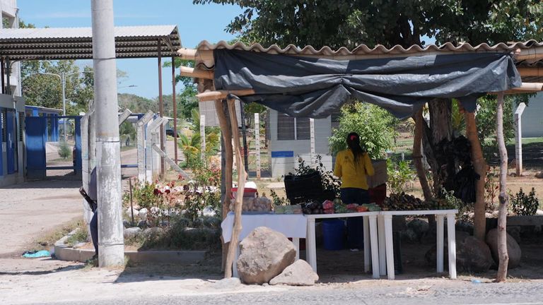 Une détenue vend des légumes en bordure d'une route surveillée par un gardien