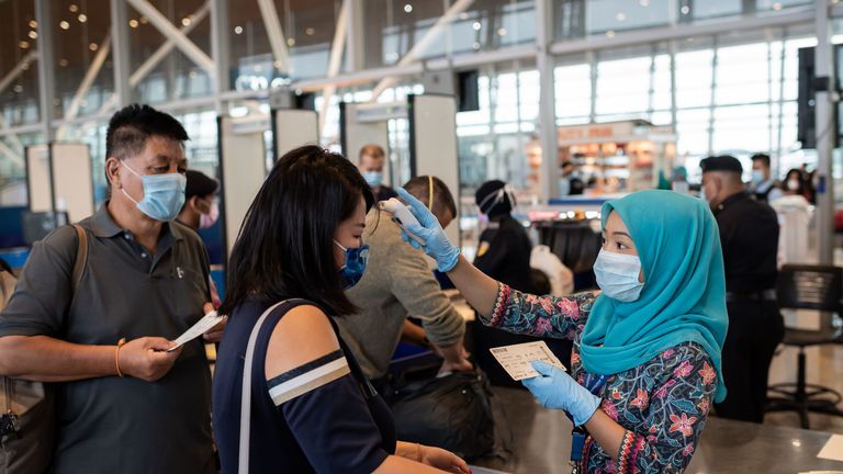 Sur cette photo prise le 14 février 2020, une hôtesse de Malaysia Airlines (R) portant un masque protecteur vérifie la température des passagers chinois avant d'embarquer sur un vol pour Pékin à l'aéroport international de Kuala Lumpur à Kuala Lumpur