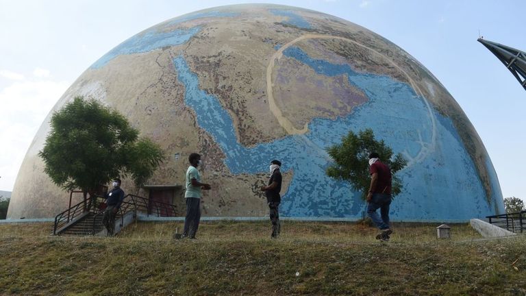 Les membres du personnel de la ville scientifique du Gujarat portant des masques se tiennent devant un modèle de la planète Terre