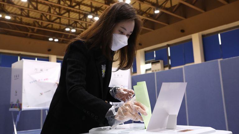 Une femme portant un masque et des gants en plastique jette son vote dans un bureau de vote à Séoul