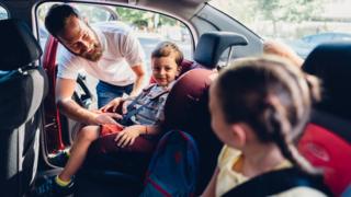 Un homme mettant ses enfants dans des sièges d'auto